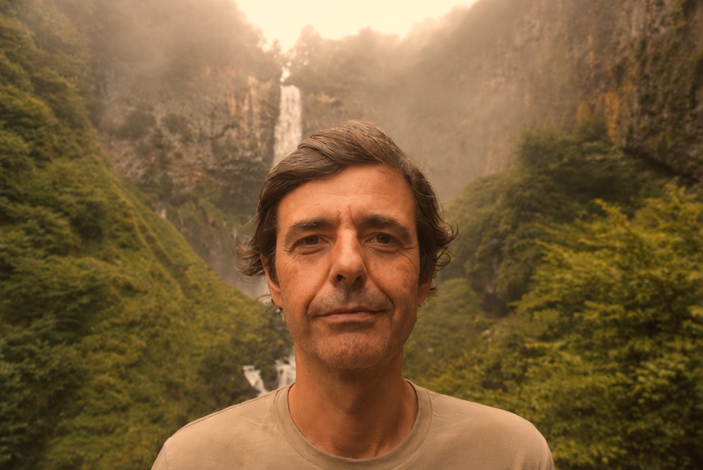 The studio's founder, standing in a green river valley below a waterfall